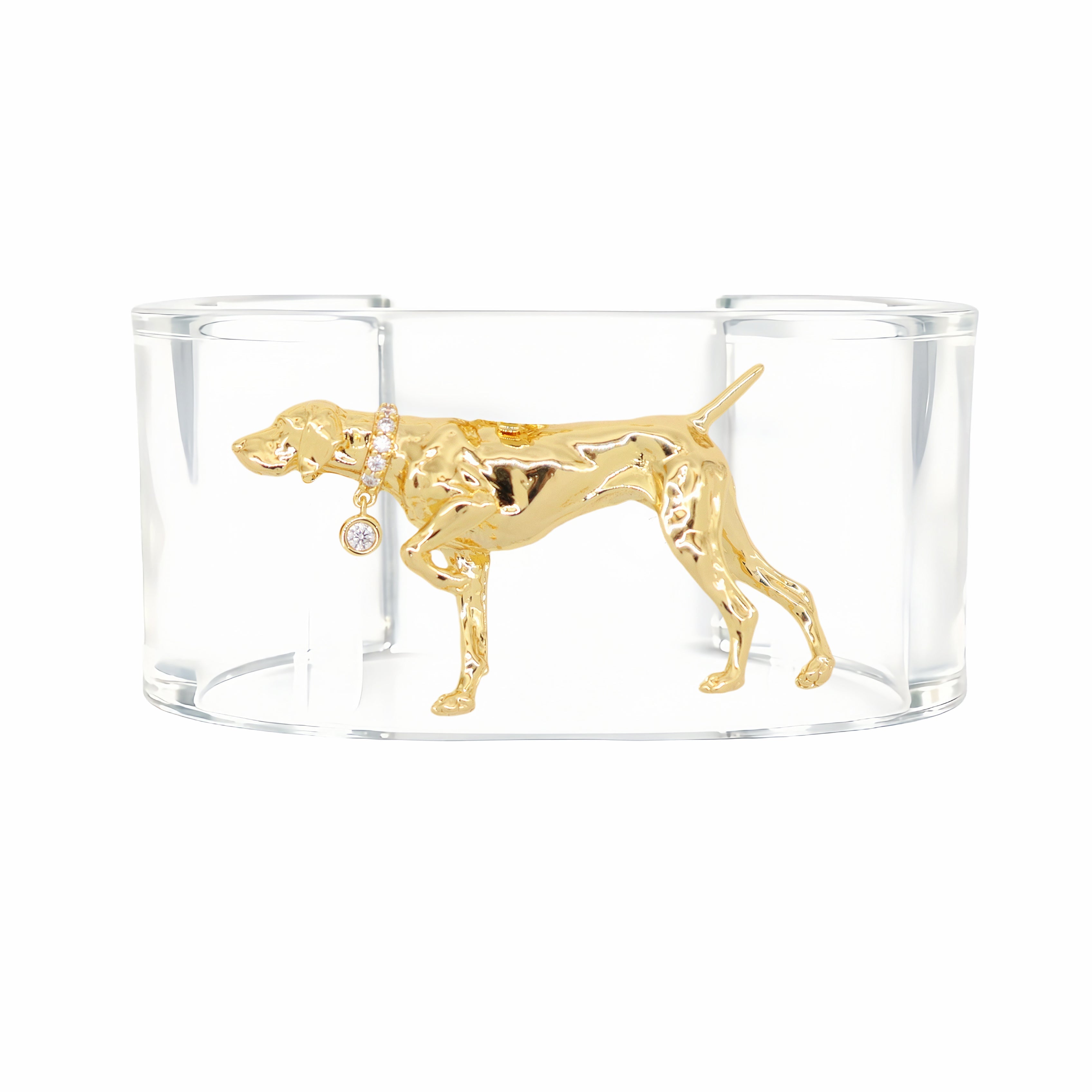 A gold-tone dog-shaped cuff bracelet with a polished finish, displayed inside a clear acrylic block on a solid white background.