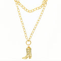 A gold-toned double-layered chain necklace featuring a small cowboy boot charm, displayed against a plain white background.