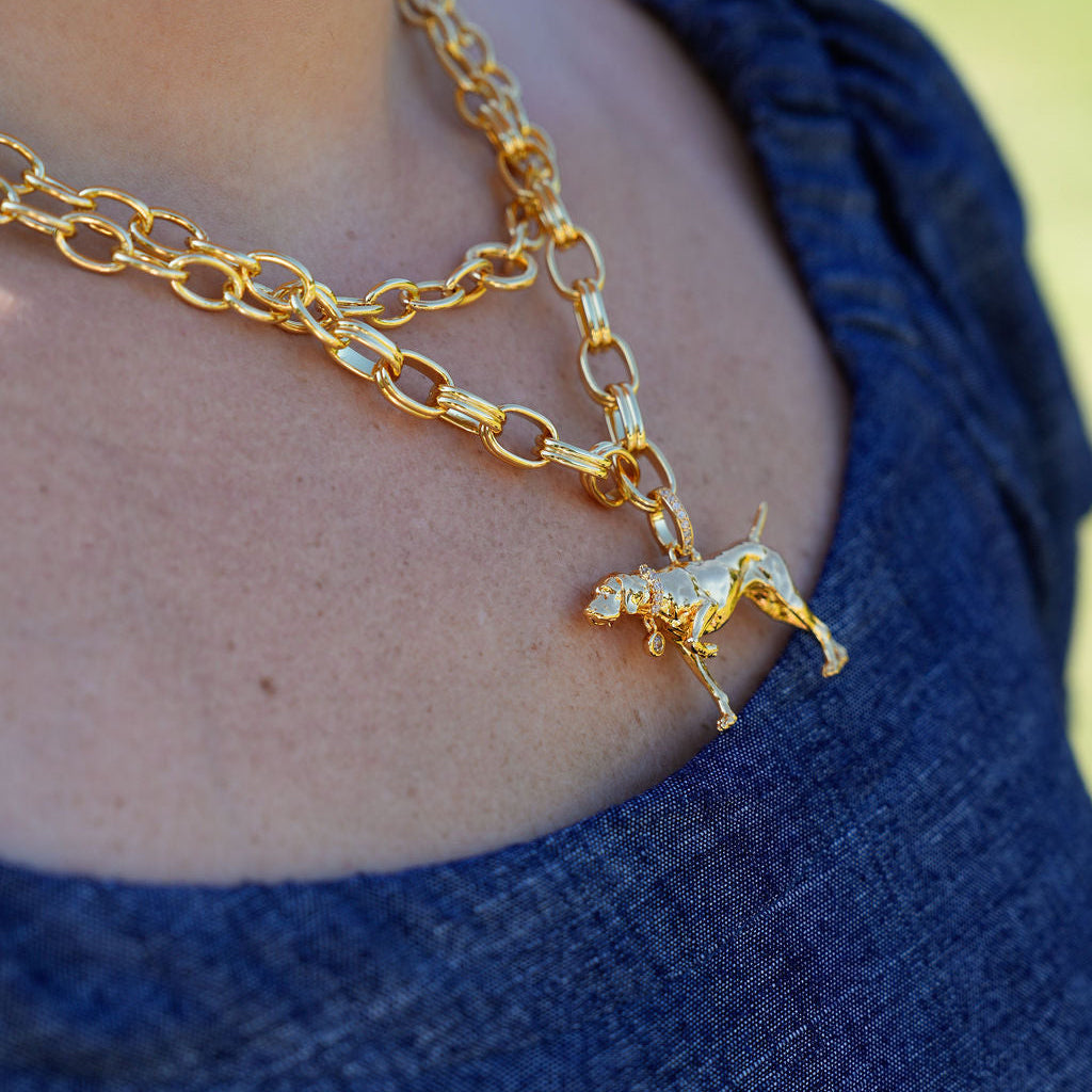 A close-up of a person wearing a layered gold necklace with a dog-shaped pendant, paired with a dark blue textured top.
