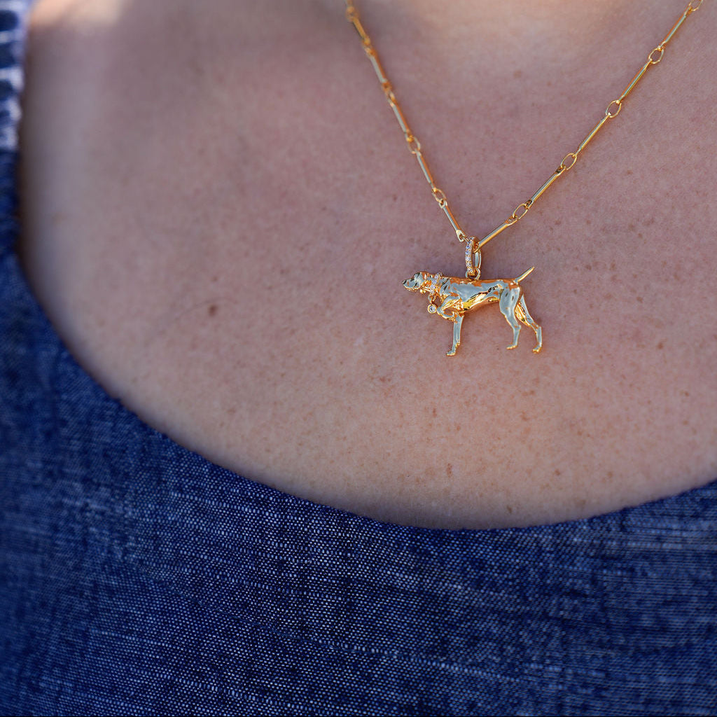 A close-up lifestyle shot of a model wearing a delicate gold chain necklace with a small dog-shaped pendant decorated with colorful enamel.