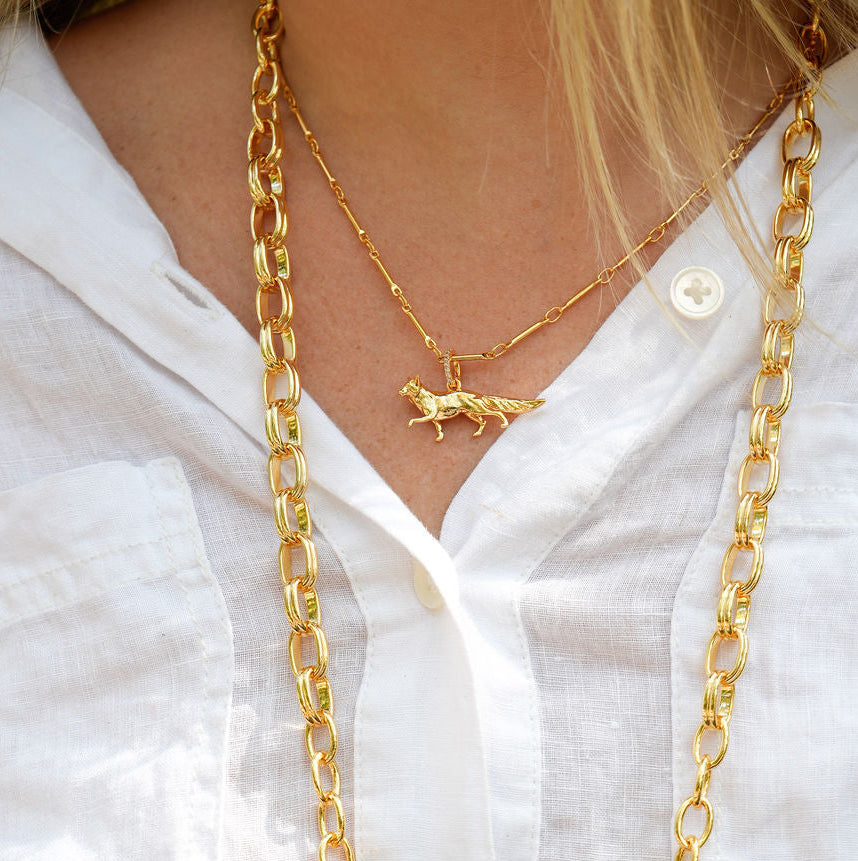 A close-up of a person wearing a long gold chain necklace with multiple small gold animal and flower charms over a white button-up shirt.
