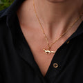 A close-up of a person wearing a delicate gold chain necklace with a small running fox pendant, styled with a black button-down shirt.