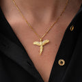 A close-up of a person wearing a gold chain necklace with a bird pendant, styled with a black button-down shirt.