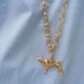 A gold-tone chain necklace with a dog-shaped pendant, displayed on a light blue fabric background.