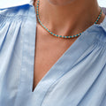 A close-up of a person wearing a delicate beaded necklace with turquoise blue and white beads, paired with a light blue blouse.
