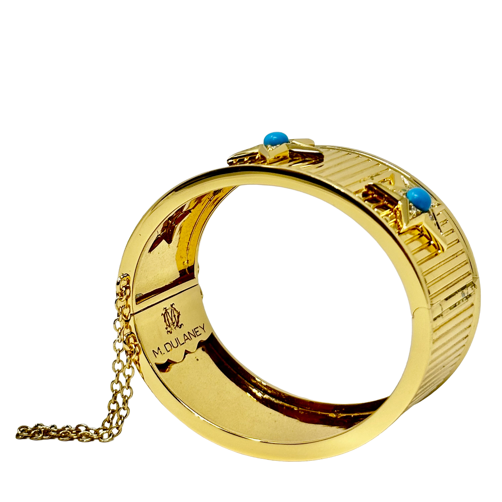 A gold-tone bangle bracelet with a textured ribbed exterior, featuring two small turquoise blue stone accents and a gold chain attached to the inside, shown on a plain white background.