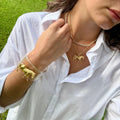 Gold horse charm hanging from a chain with grass in the background