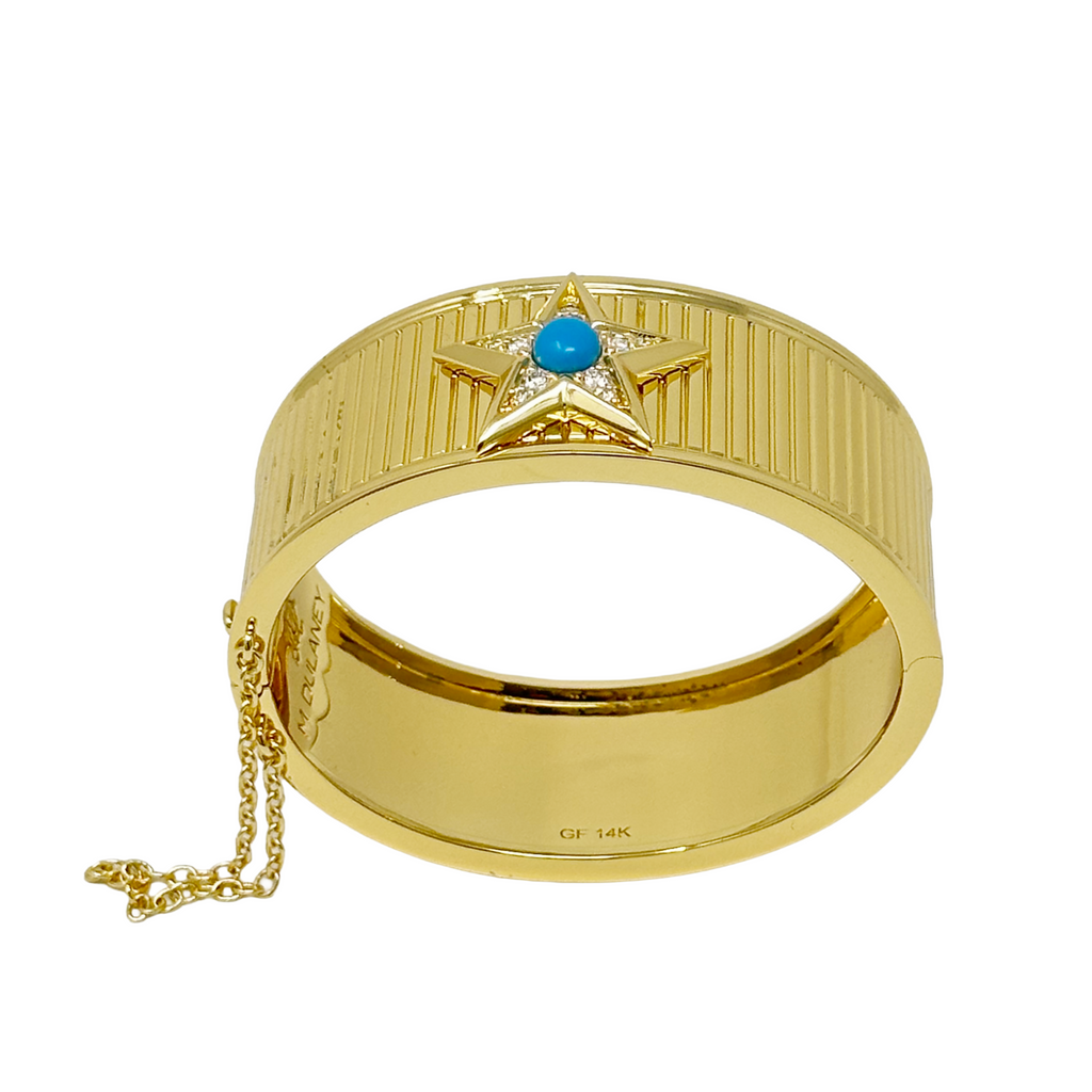 A gold cuff bracelet featuring a star-shaped centerpiece with a small turquoise blue stone and clear crystals, shown on a plain white background.