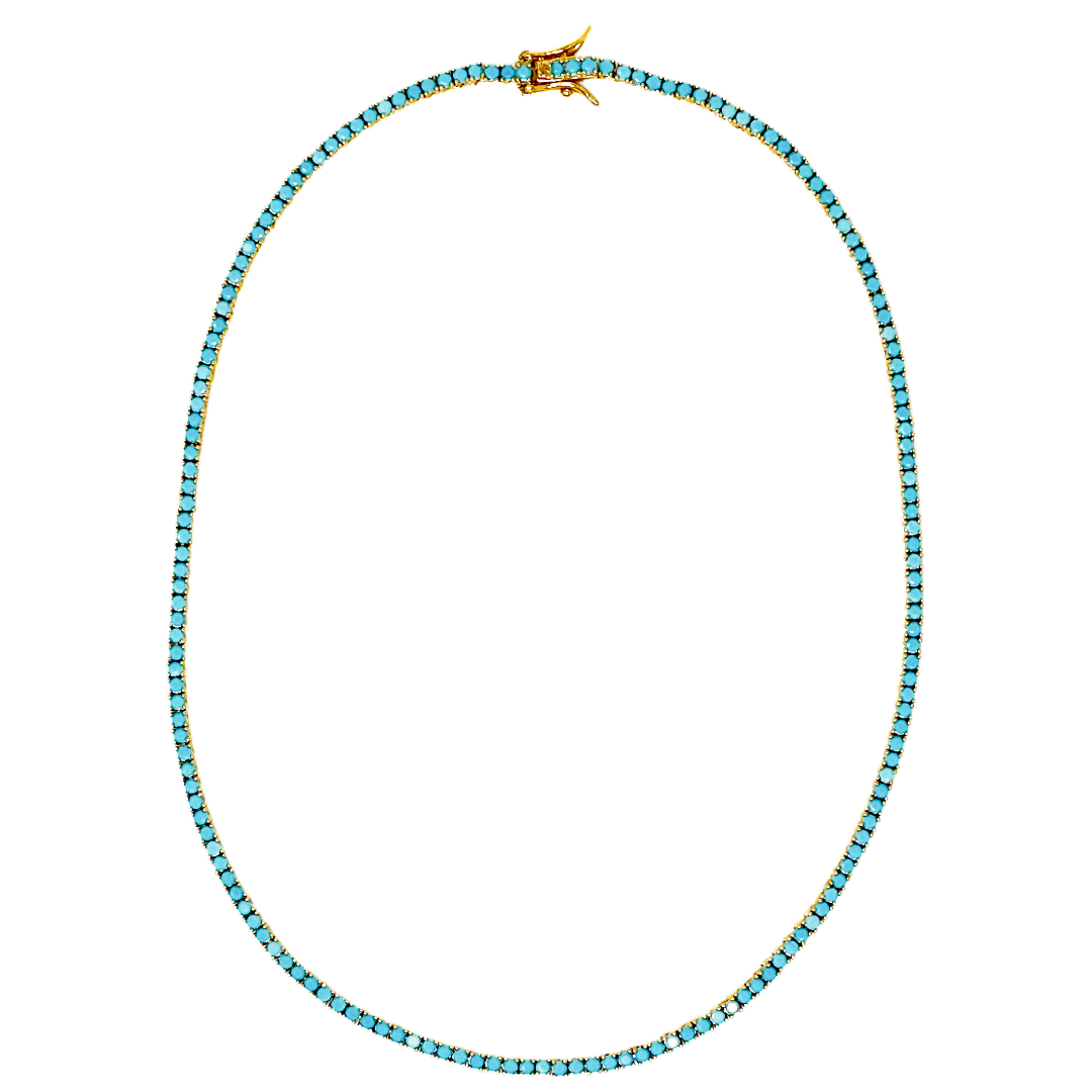 A delicate tennis-style necklace featuring small, round-cut light blue stones set in yellow gold, with a matching gold lobster clasp, shown against a plain white background.